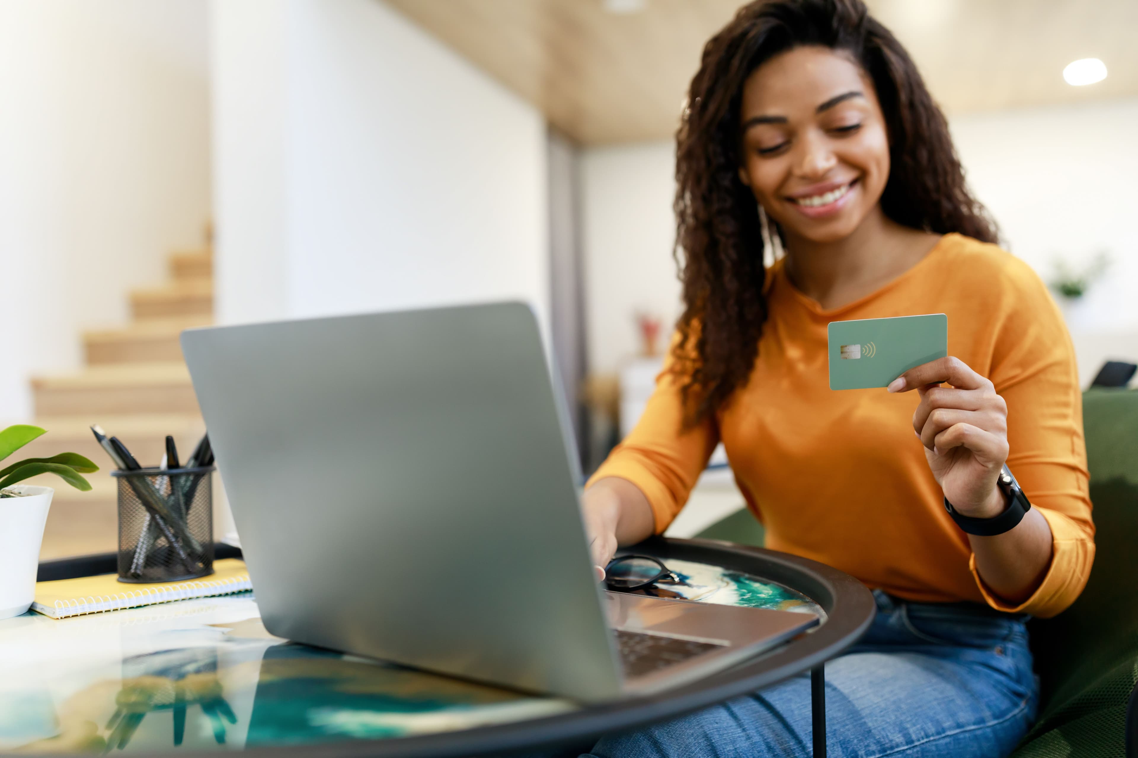 Happy woman holding debit credit card using pc